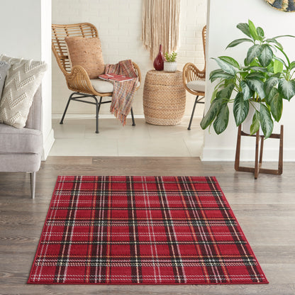 Red plaid area rug with black and white stripes on wood floor; cozy living room with wicker chairs and a potted plant.