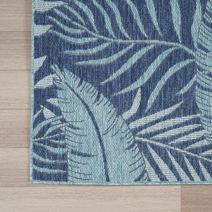 Rectangular woven rug with navy blue background and light teal tropical leaf pattern on wood floor.