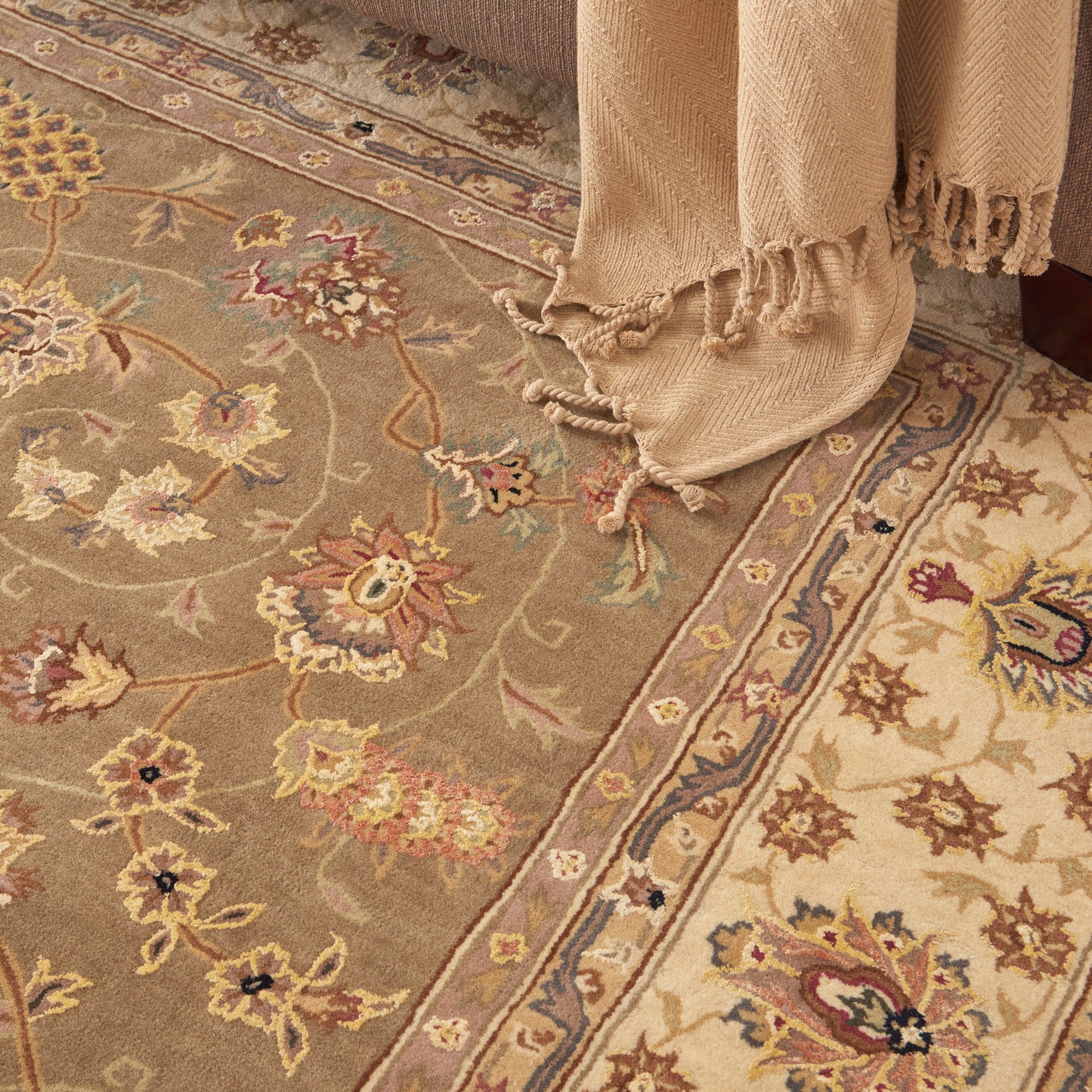 Soft beige floral area rug with an ornate border in cream, pink, and blue; fringed edges.