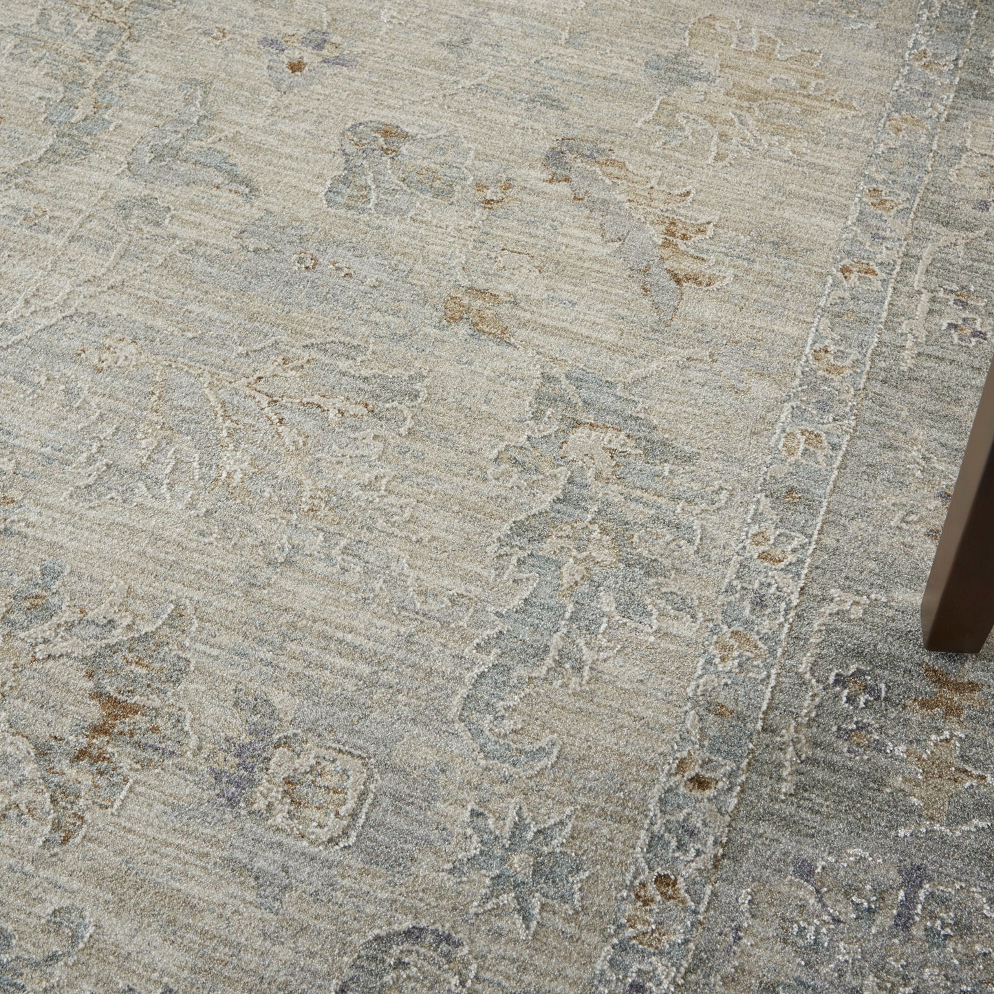 Muted grey-beige rug with subtle floral and geometric border; table leg visible on the right.