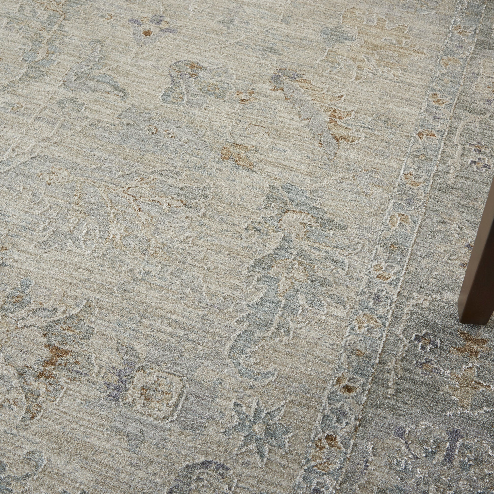 Muted grey-beige rug with subtle floral and geometric border; table leg visible on the right.