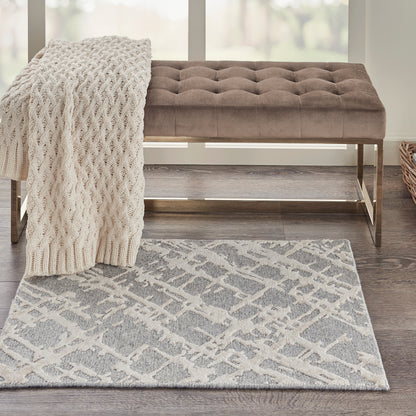 Taupe tufted velvet bench with a gold metal frame, ivory chunky knit throw draped over it, and a gray-cream geometric rug.