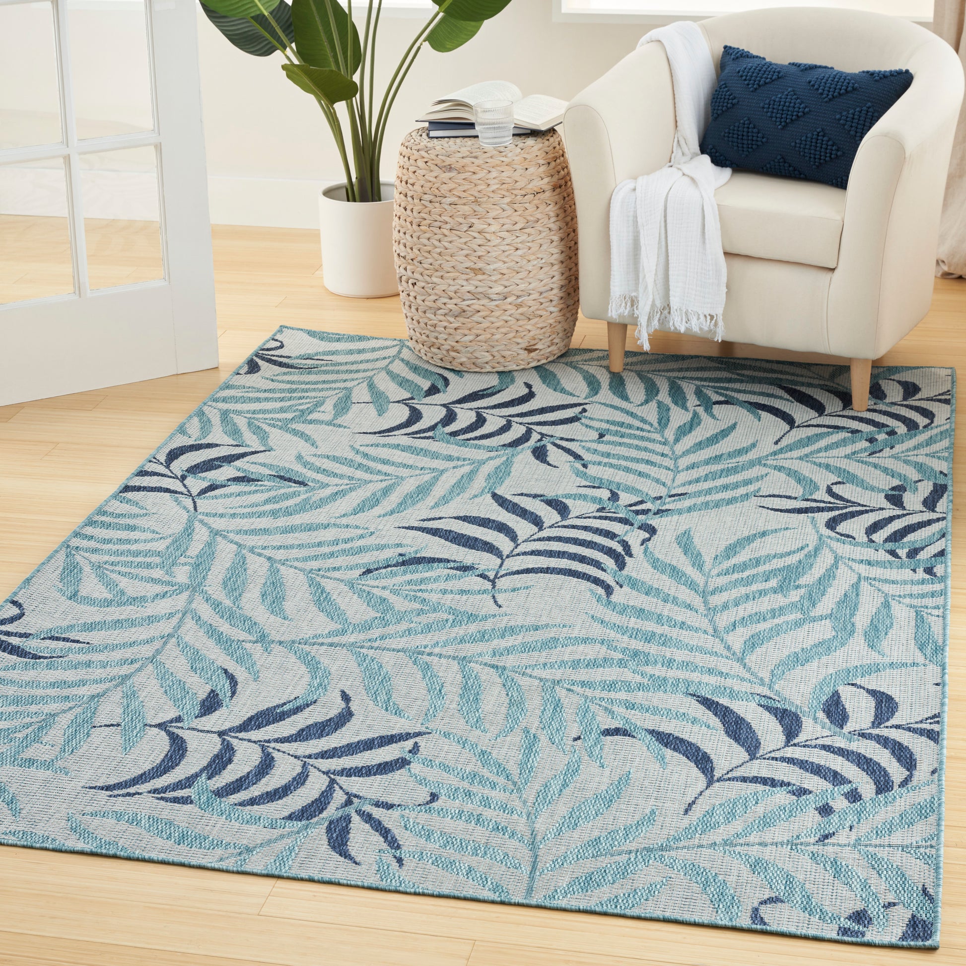 Blue tropical leaf-pattern area rug on light wood floor beside a cream armchair.