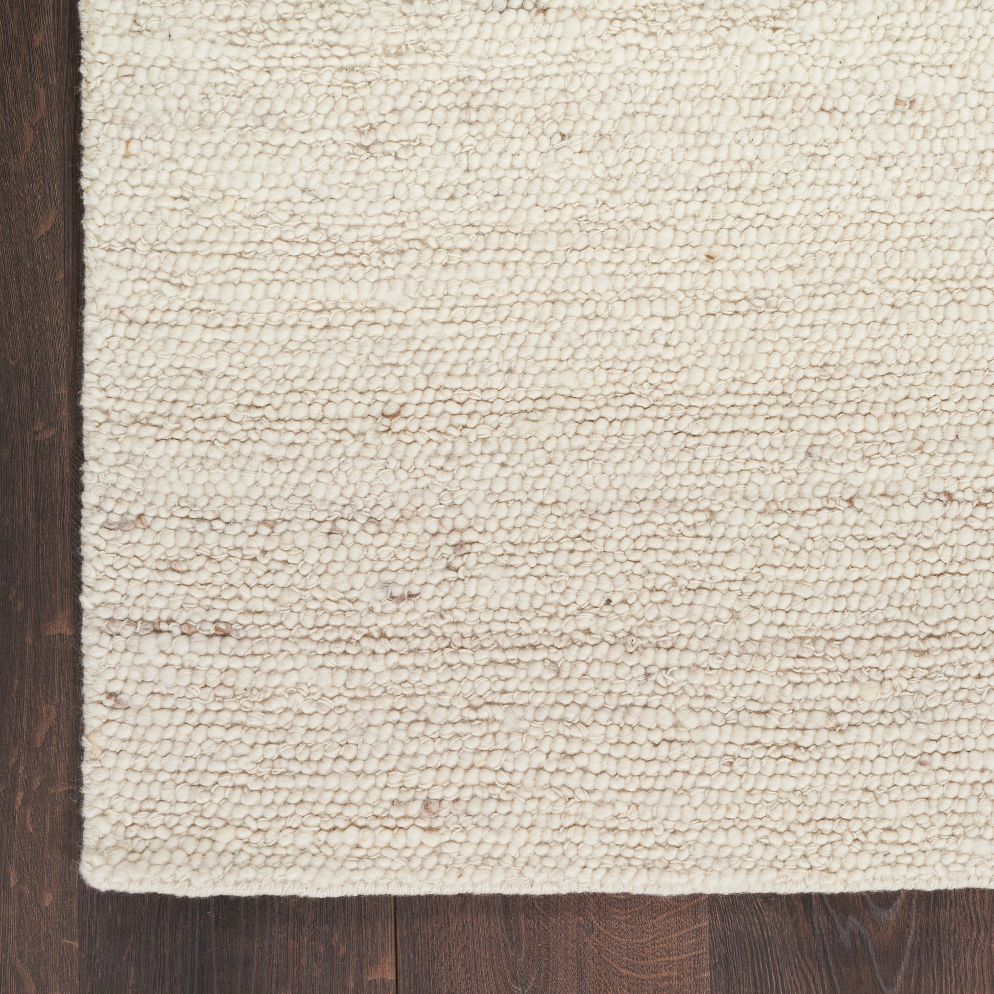 Cream loop-pile rug edge on dark wood floor; close-up corner shows textured ivory fibers.