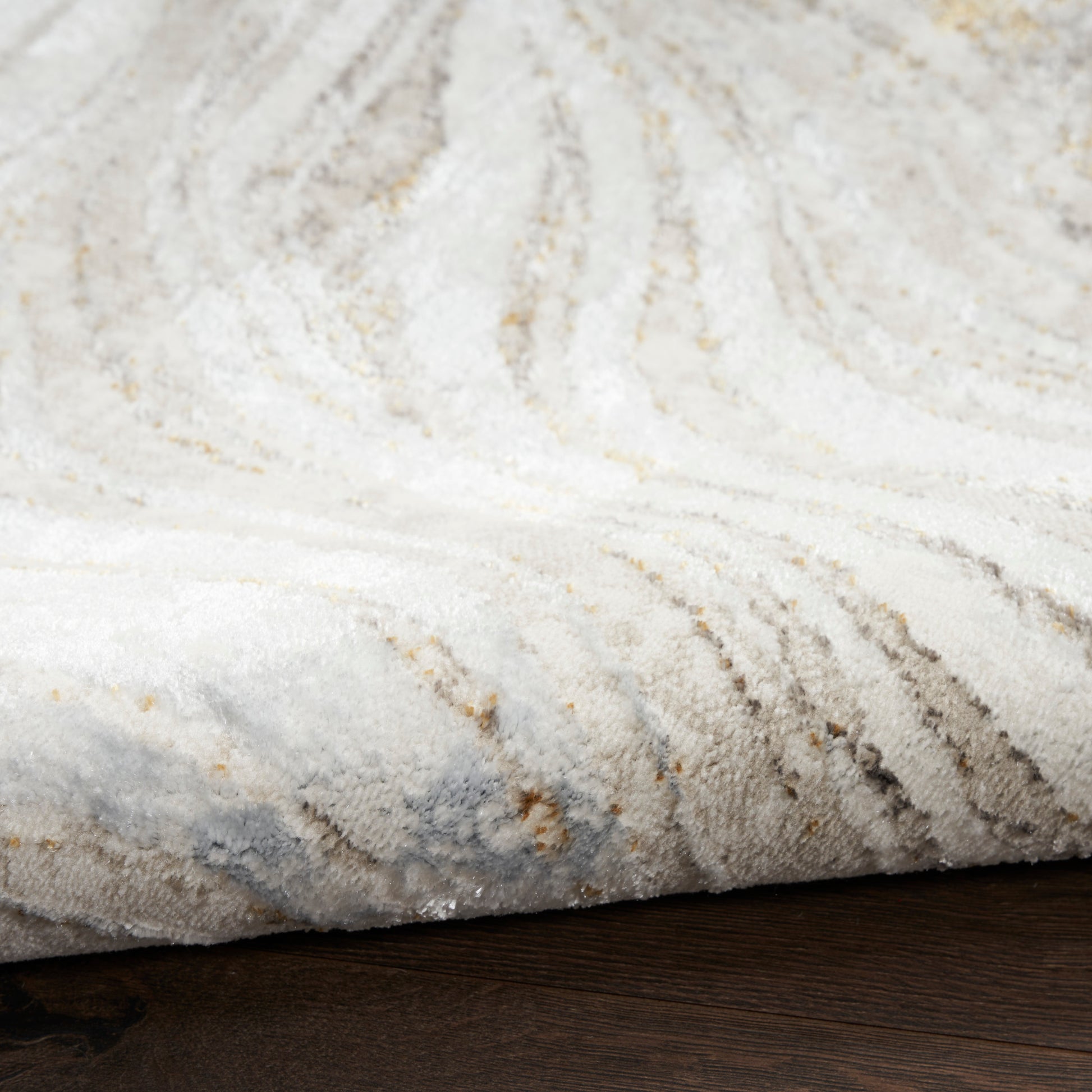 Plush cream rug with pale gray and gold veining on dark wood floor, folded edge.