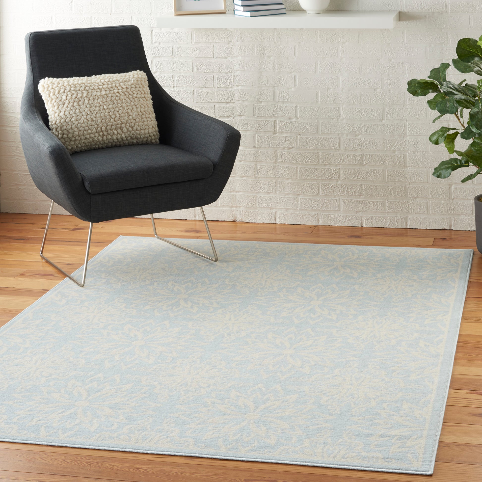 Dark gray armchair with a beige textured pillow, placed on a pale blue patterned rug over a wooden floor.