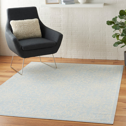 Dark gray armchair with a beige textured pillow, placed on a pale blue patterned rug over a wooden floor.