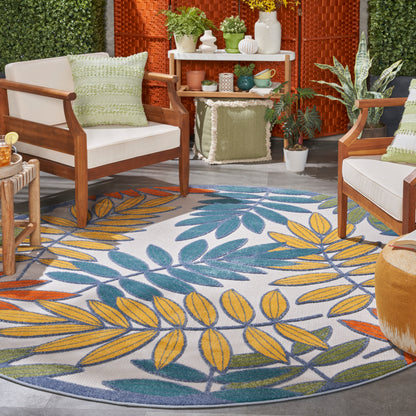 Round outdoor rug with blue, yellow, and green tropical leaf pattern.