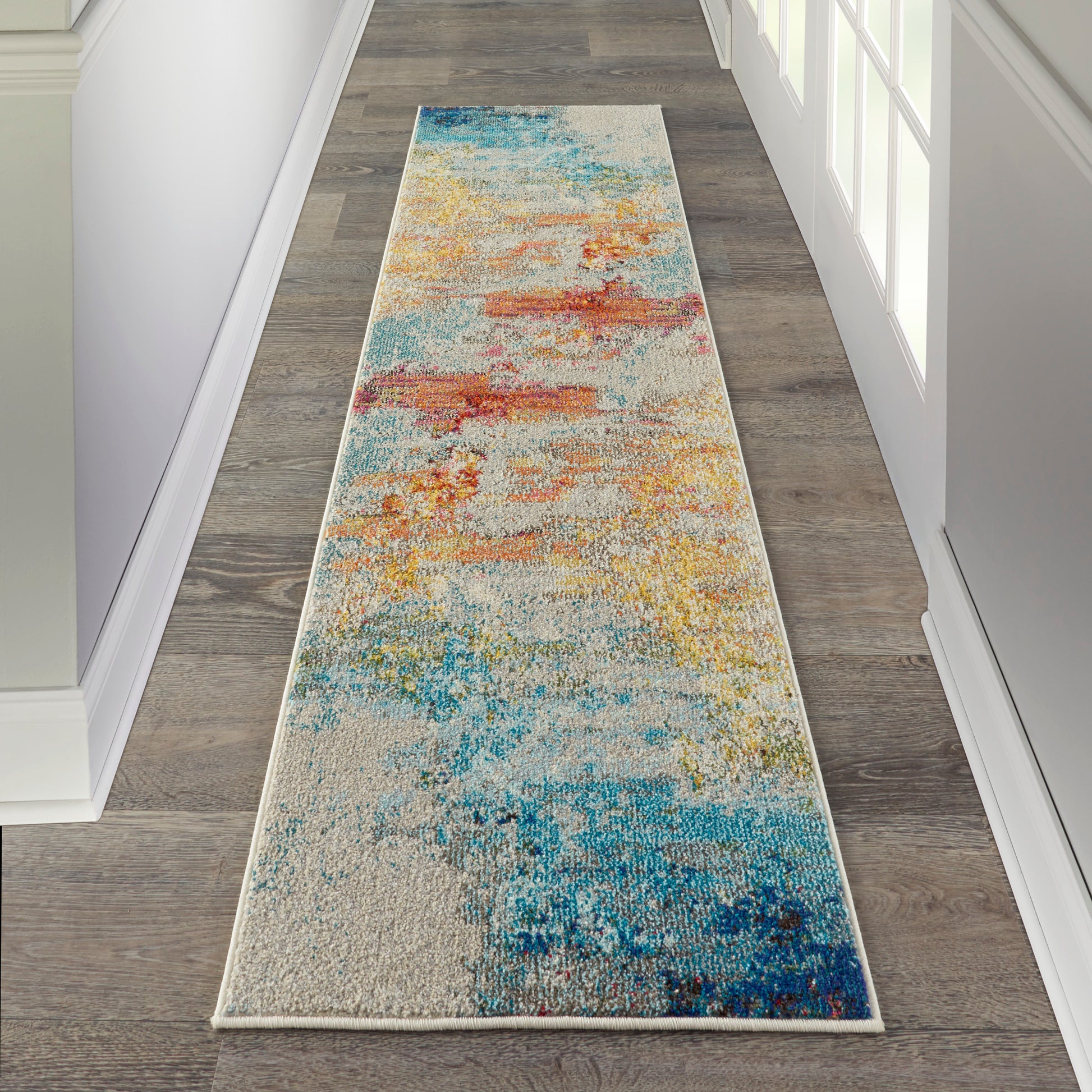 Long hallway runner rug with abstract multicolor pattern: blues and teals fade to oranges, yellows on a cream base.