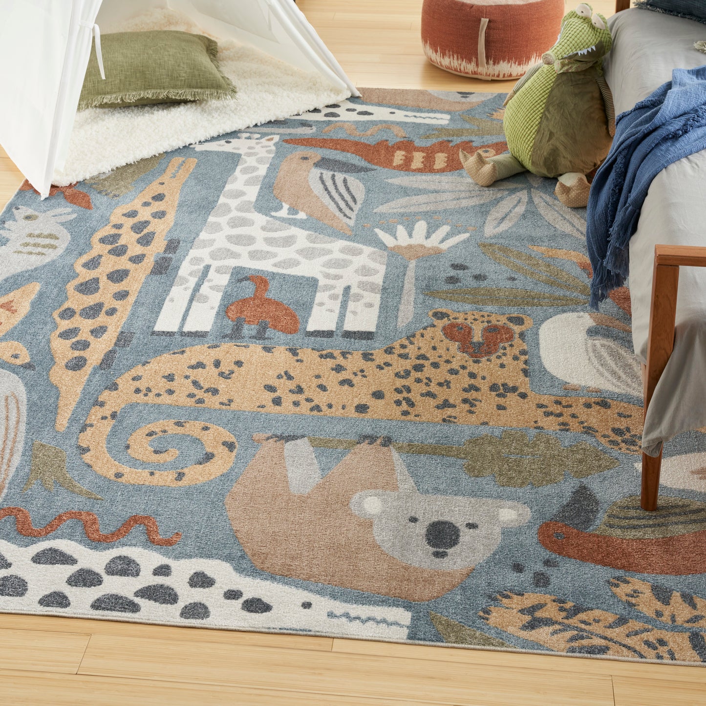 Colorful kids' area rug with animal motifs (giraffe, bear, elephant) in blues and tans; plush, cozy playroom decor.