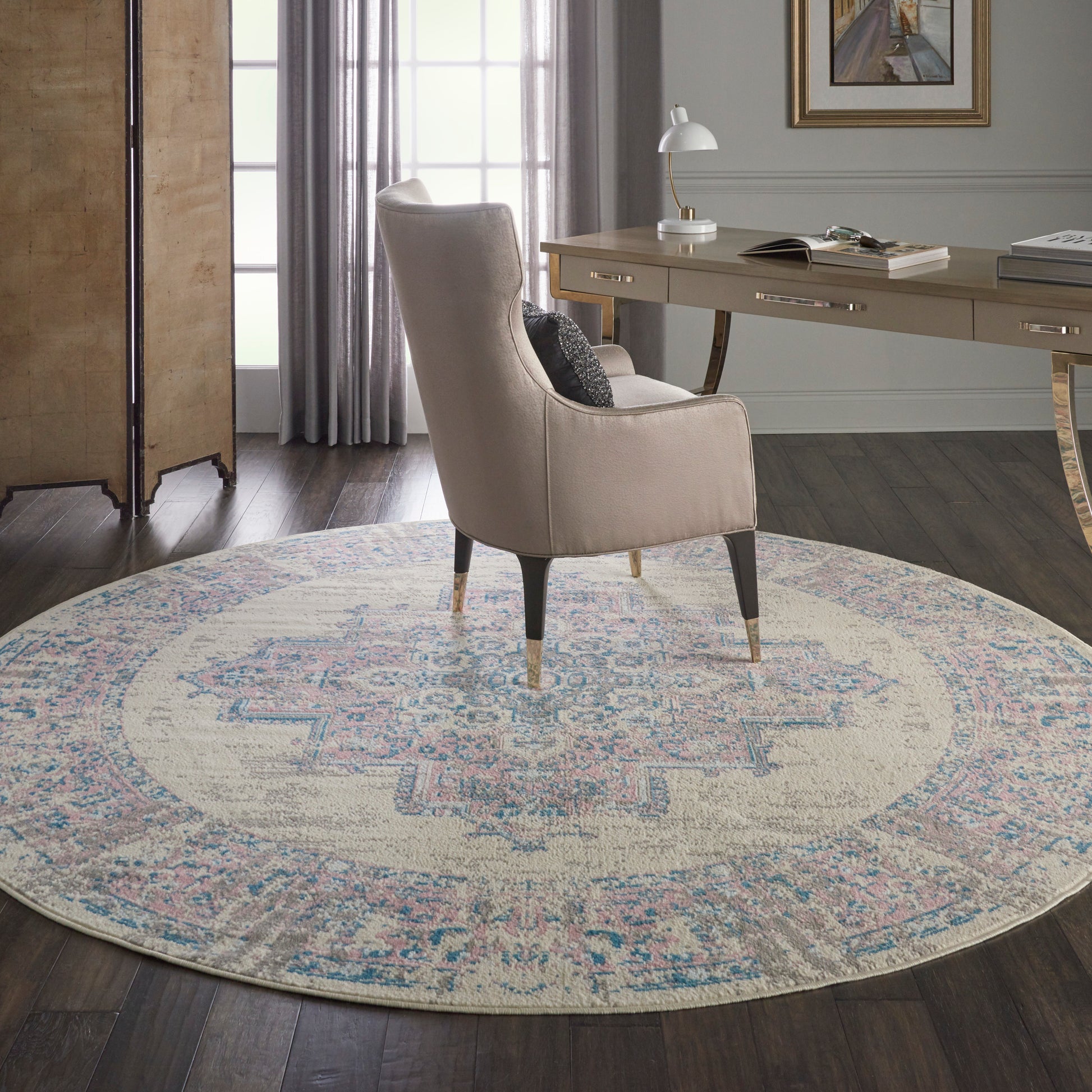 Beige fabric armchair with tapered legs on a round pastel rug with blue-pink pattern in a chic home office.