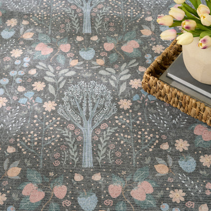 Blue-gray rug with tree and floral motifs in pink, peach, and light blue; woven texture beside a wicker tray with tulips.