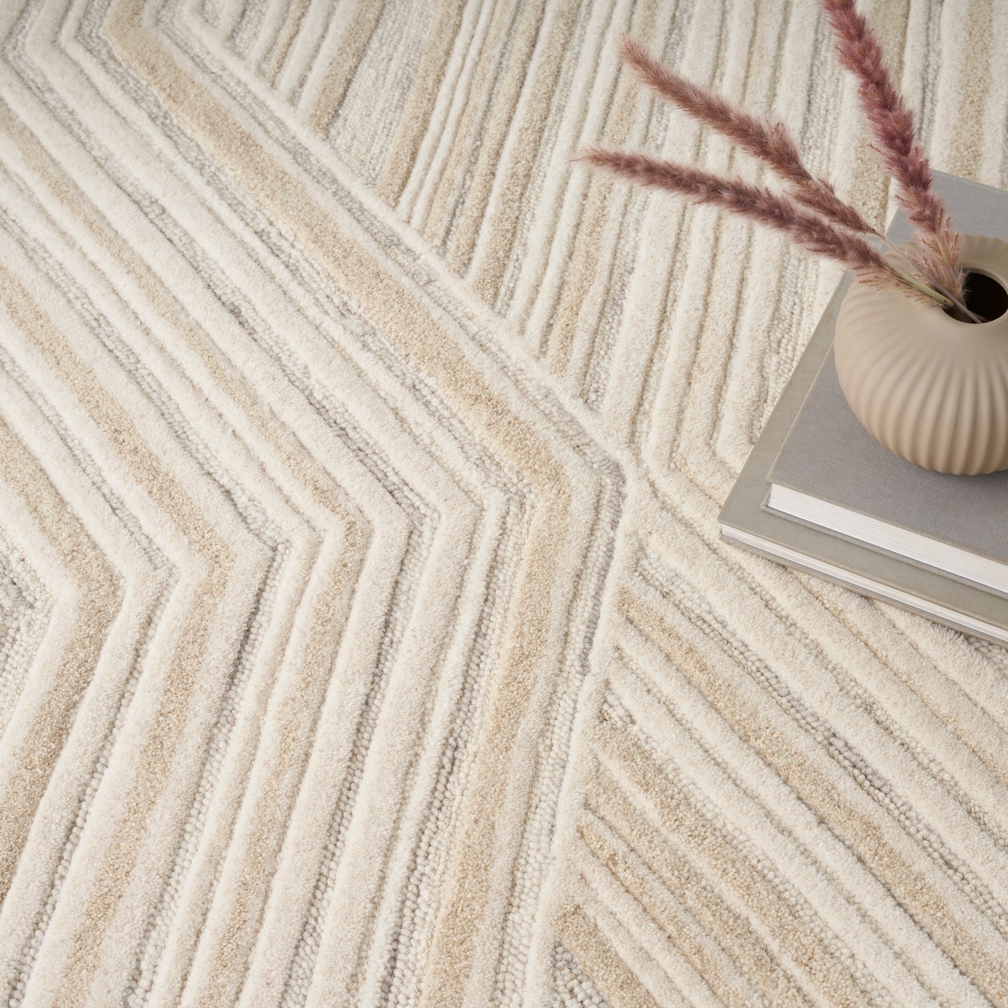 Beige chevron rug with cream & taupe tones, paired with a ribbed ceramic vase & pampas grass on books.
