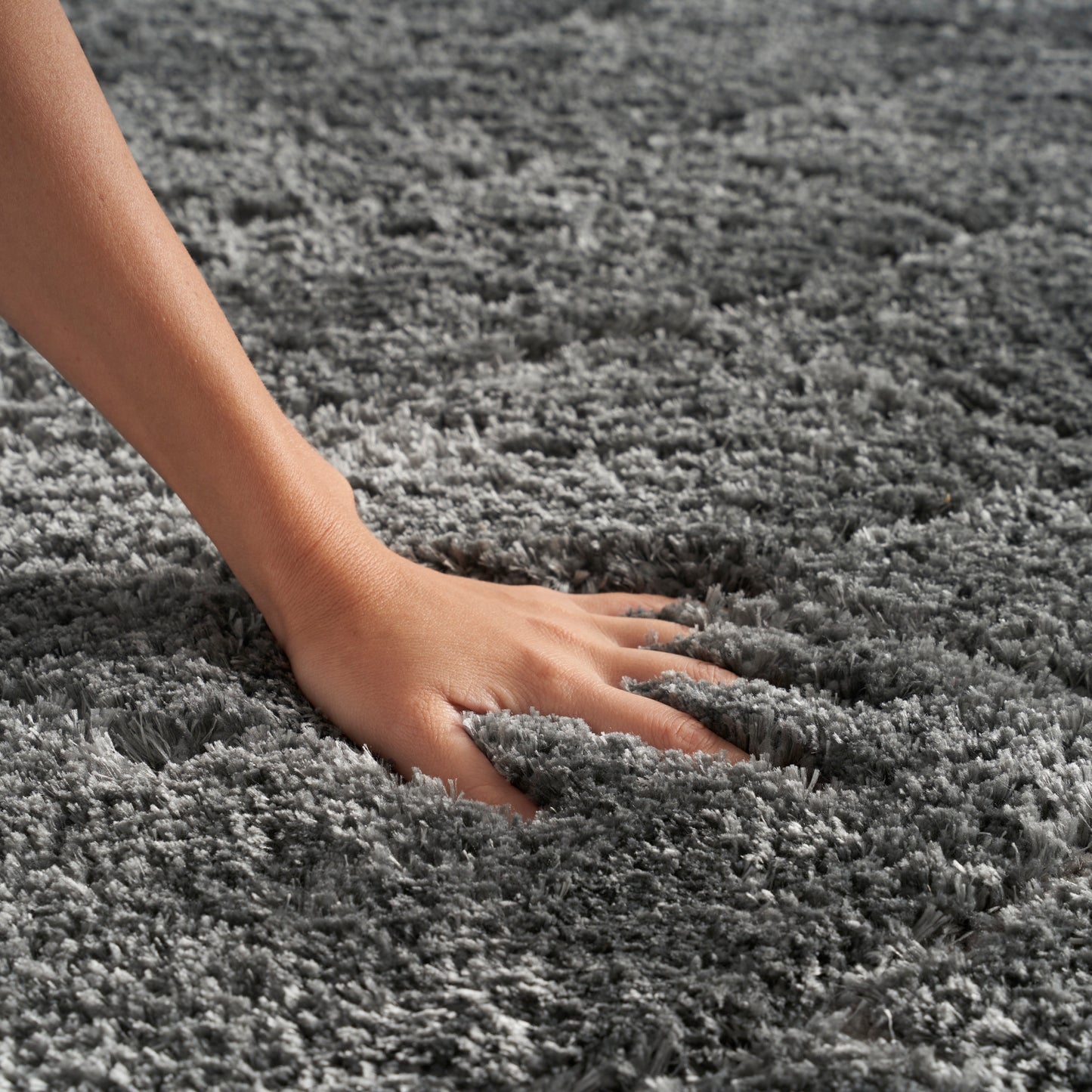Close-up of a hand pressing into a soft gray shag rug with thick plush fibers.
