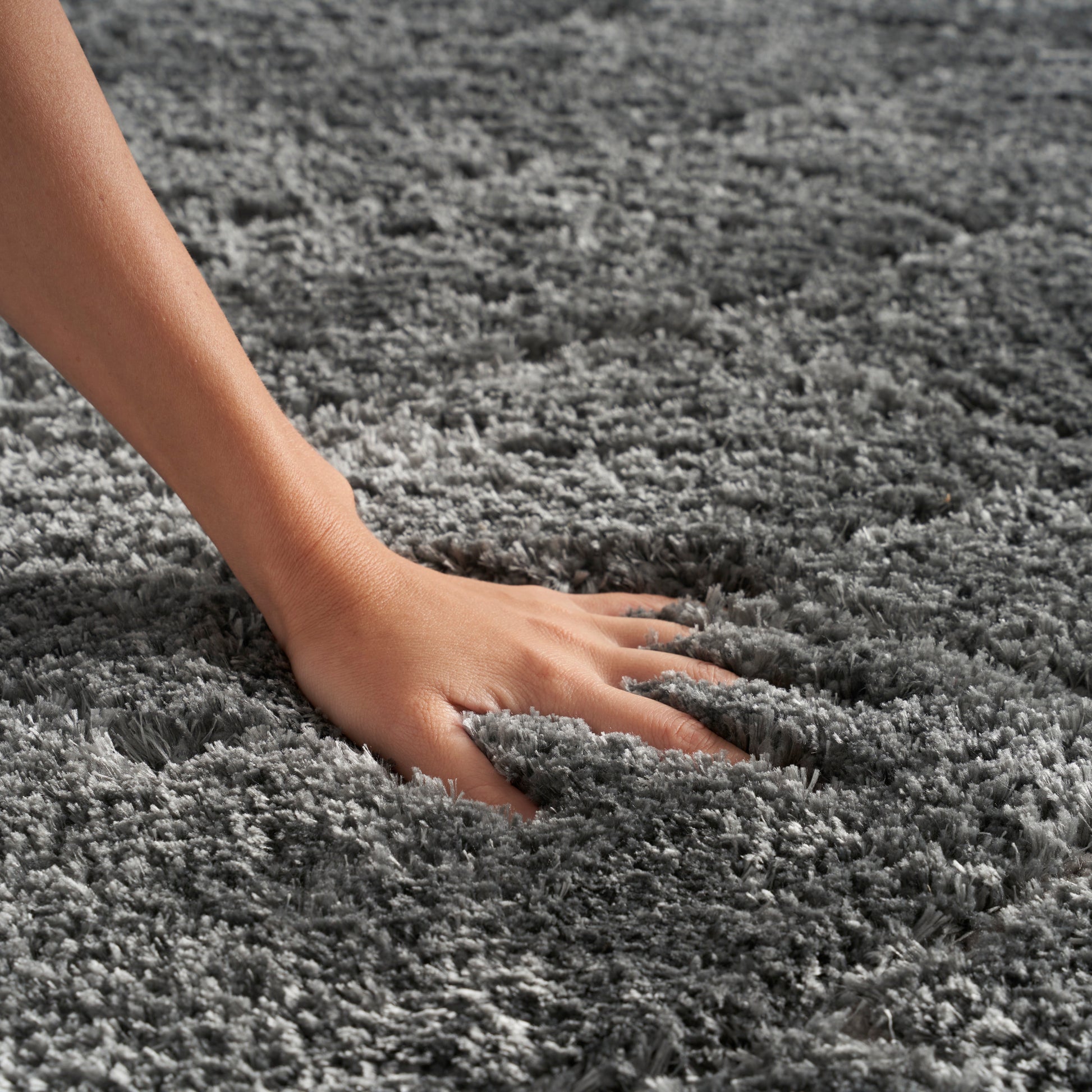 Close-up of a hand pressing into a soft gray shag rug with thick plush fibers.