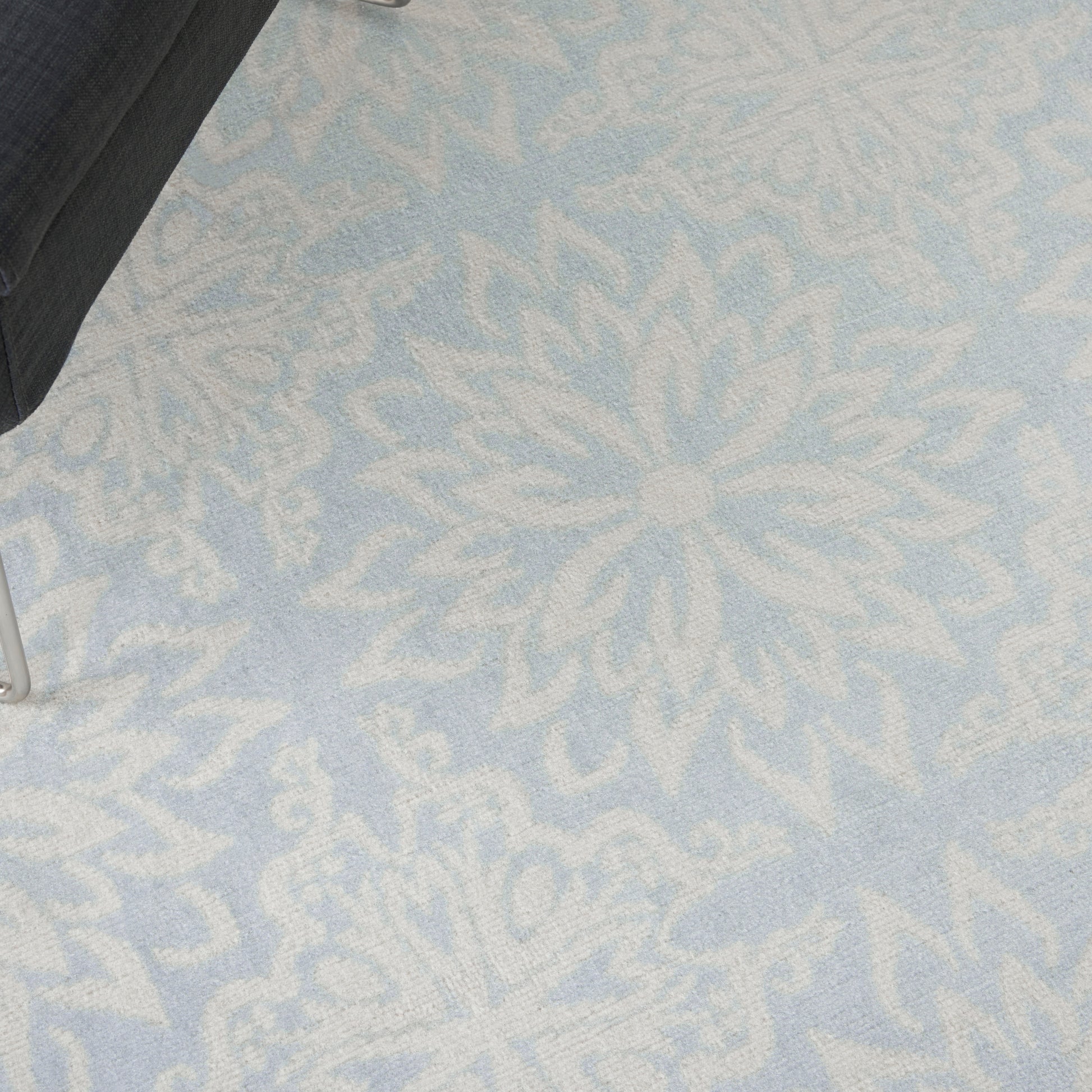 Light blue rug with large white floral mandala motif; black chair leg visible in the corner.