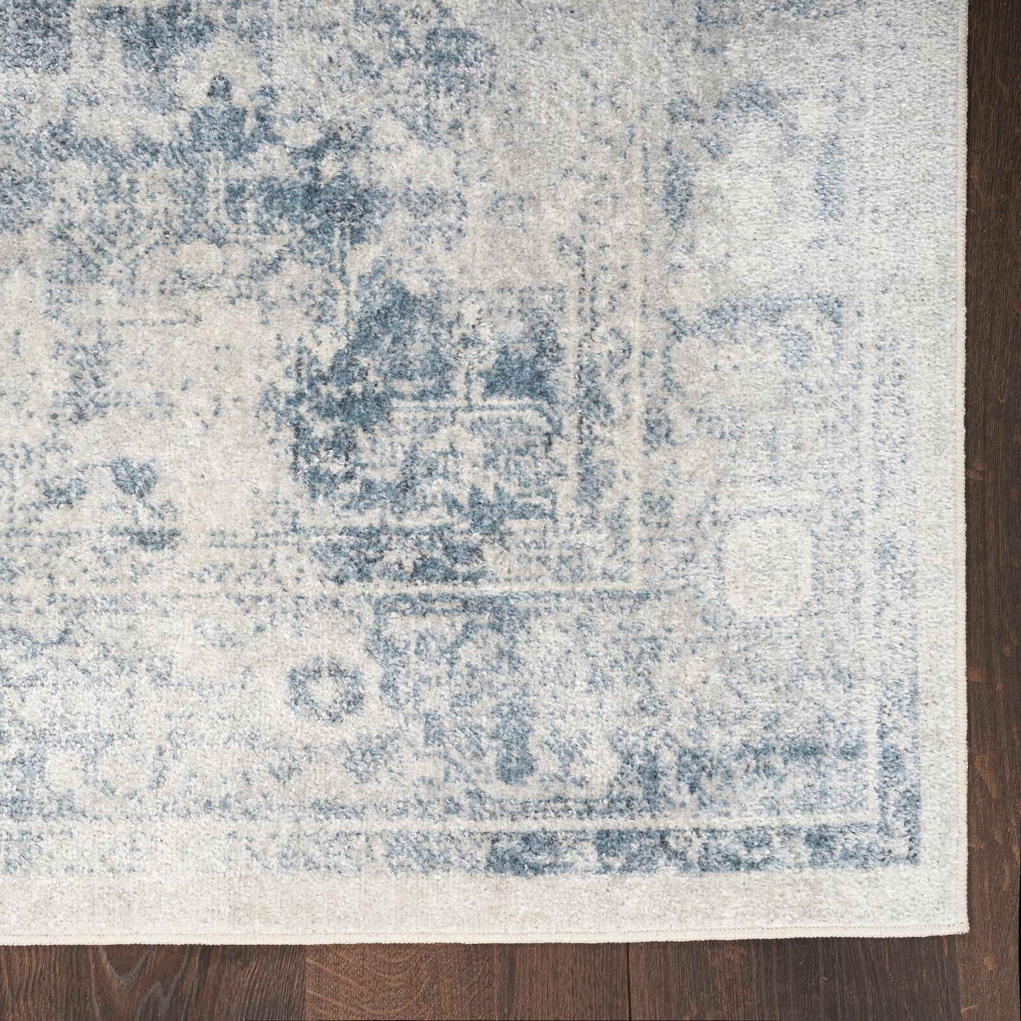 Distressed blue and ivory oriental rug with faded border on dark wood floor.