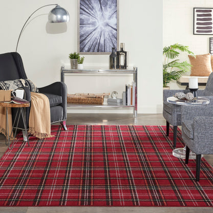 Cozy modern living room with red plaid rug, black armchair, chrome console, gray seating, and green plant accents.
