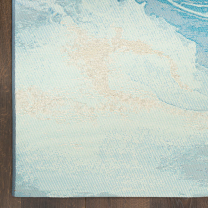 Light blue woven rug with beige abstract pattern on dark wood floor; textured coastal style.