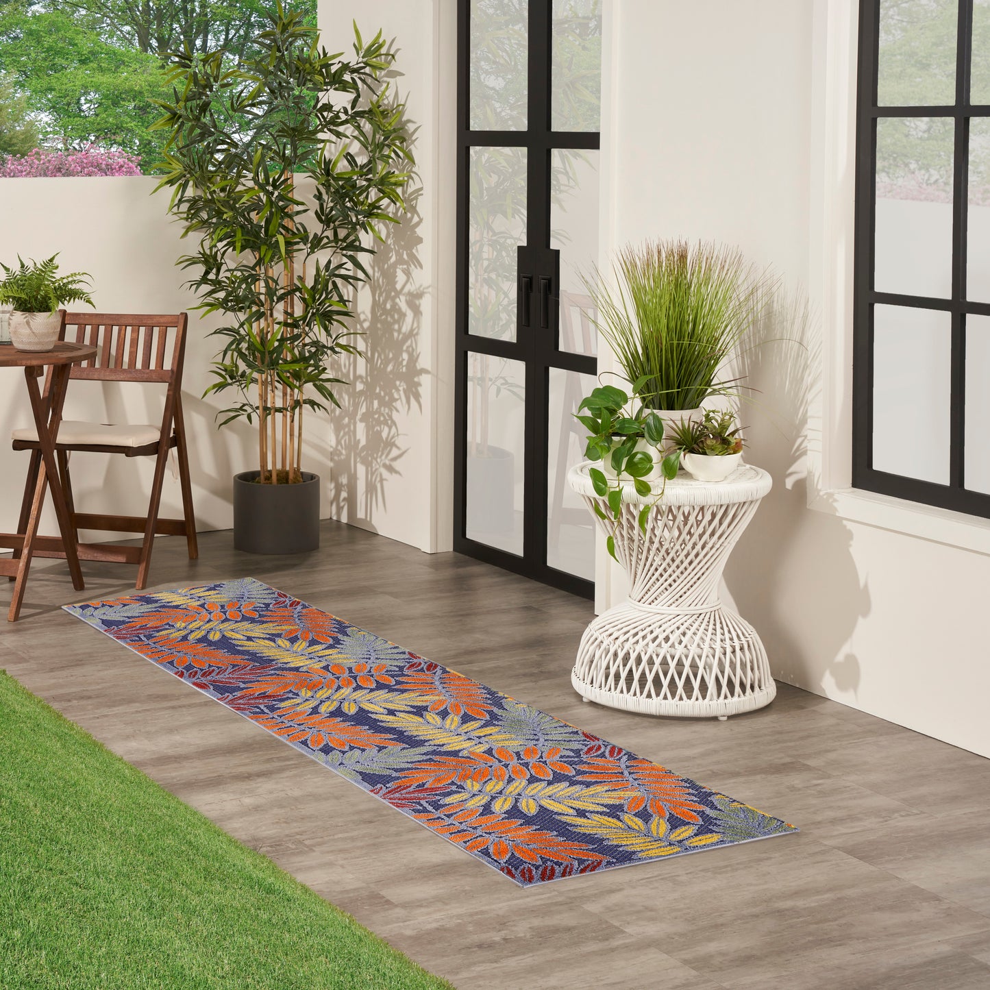 Blue tropical leaf runner rug with orange leaves on a wooden patio near glass doors; indoor-outdoor decorative rug.