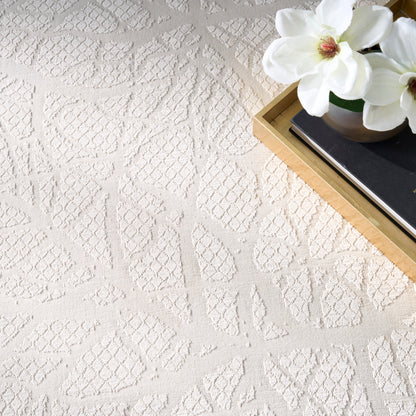 Cream textured rug with geometric leaf patterns; top-right wooden tray, black book, and white magnolia flowers.