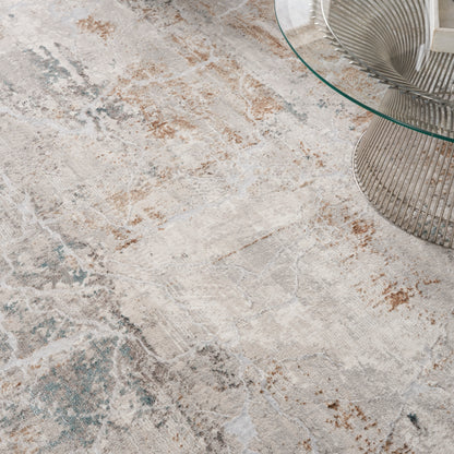 Abstract beige area rug with cream, taupe and teal accents beside a round glass coffee table with a metal wire base.