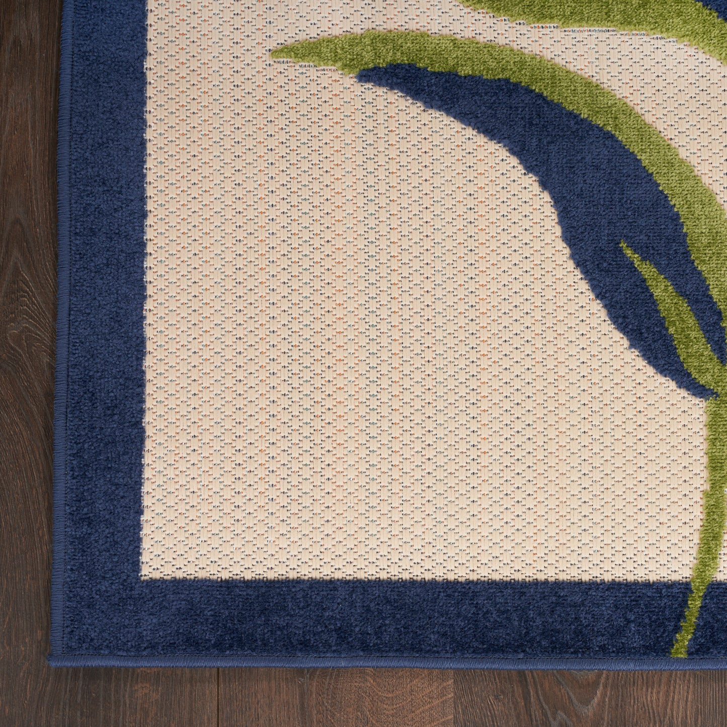 Rectangular beige rug with dark navy border and a blue-green curved motif on a wood floor.