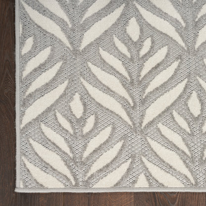 Grey and off-white leaf-pattern area rug with textured weave and light border on wood floor.