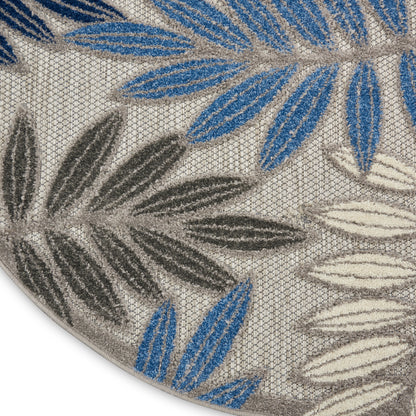Round beige rug with blue, gray and ivory palm leaf motifs; textured looped pile.