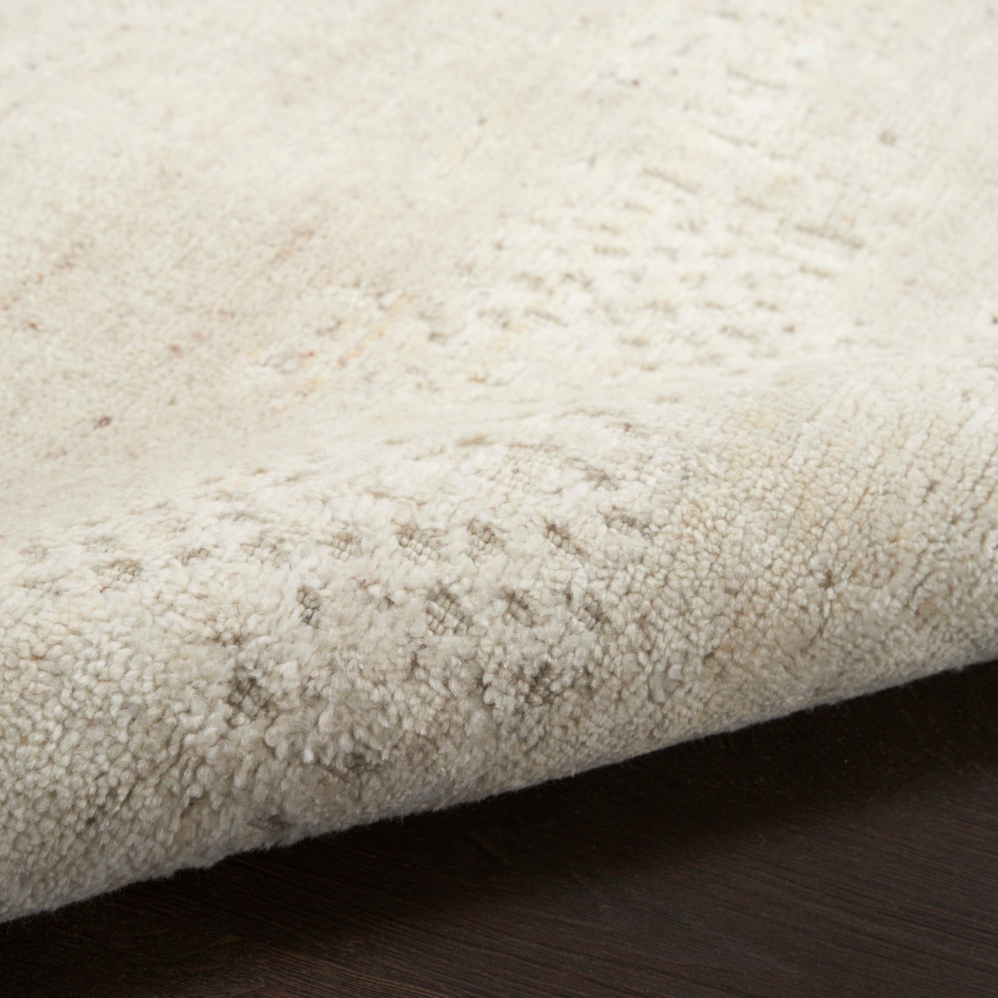 Beige textured rug with plush, dense loop pile; edge folded over dark wood floor.