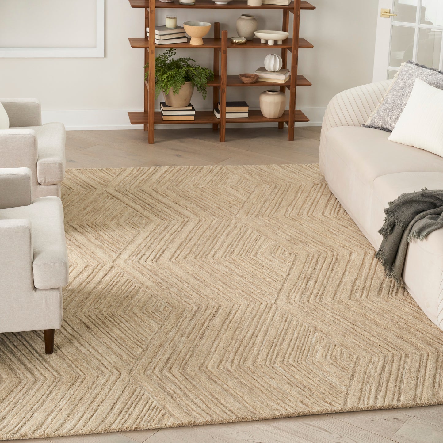 Beige jute rug with a subtle chevron pattern anchors a neutral living room with light gray sofas and a wooden open shelf.