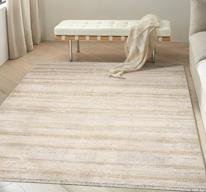 Neutral rectangular area rug with beige and gray stripes and fringe, in a modern living room beside white tufted bench.