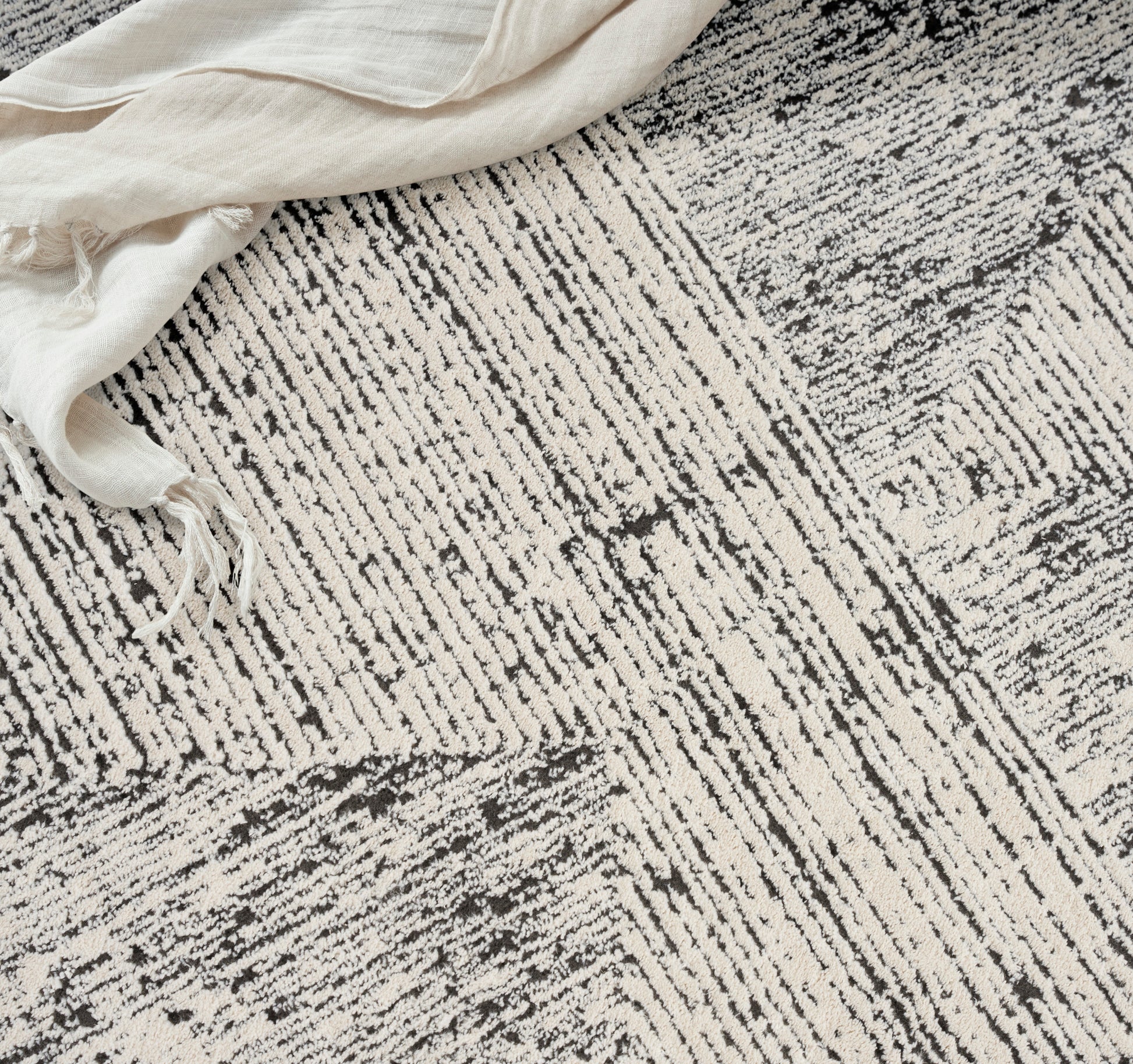 Beige and gray textured rug with abstract linear pattern and cream linen cloth draped over the top-left corner.