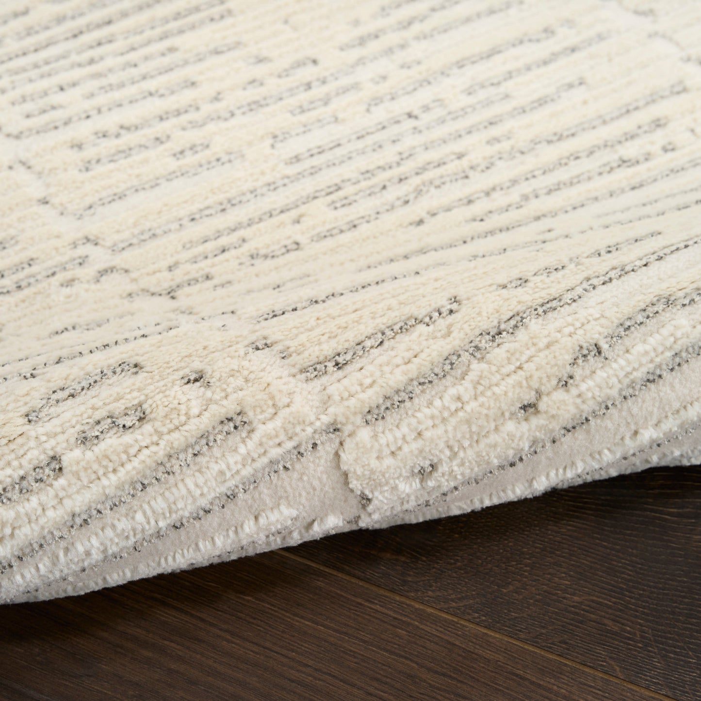 Cream textured area rug with subtle gray geometric pattern and plush pile on dark hardwood floor.