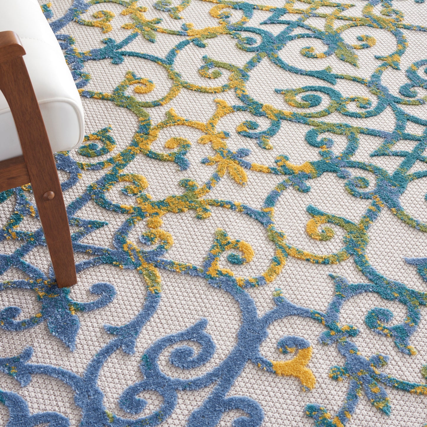 Blue and yellow ornate scrolling rug on beige woven background; wood chair leg nearby.