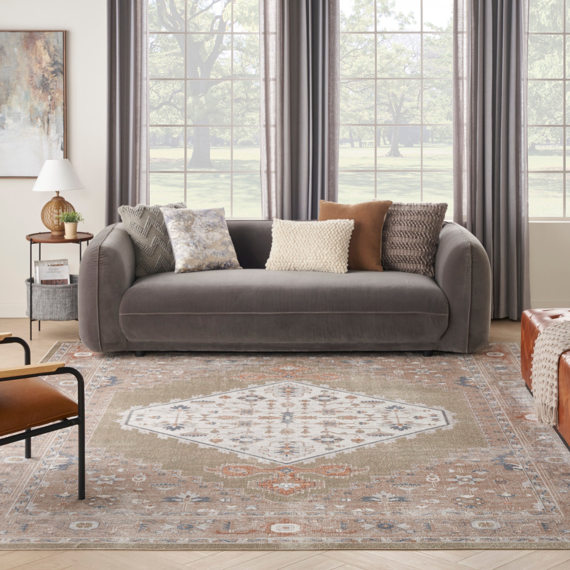 Gray velvet sofa with textured cream and beige pillows; large window with gray drapes; patterned rug and central medallion.