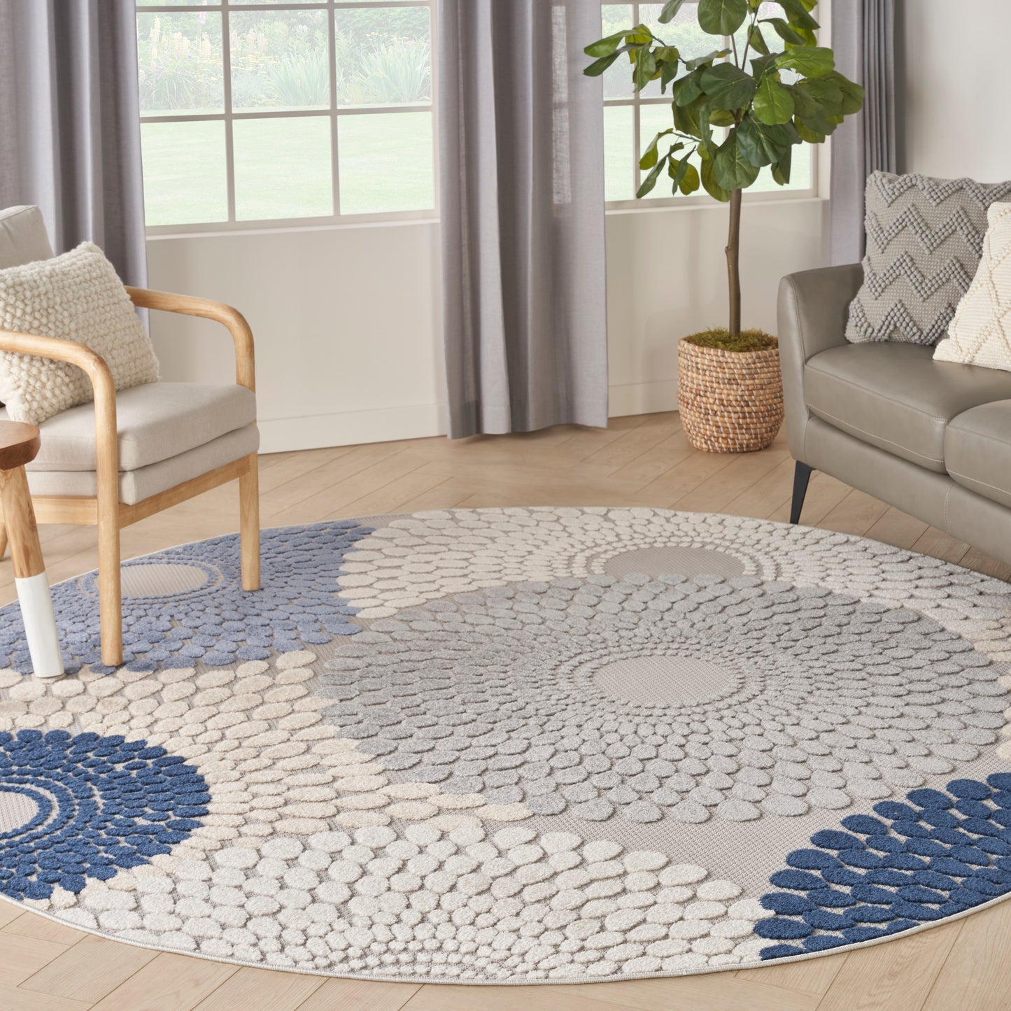 Round area rug with concentric blue and beige circles on light wood floor; modern living room with sofa, armchair, and plant.