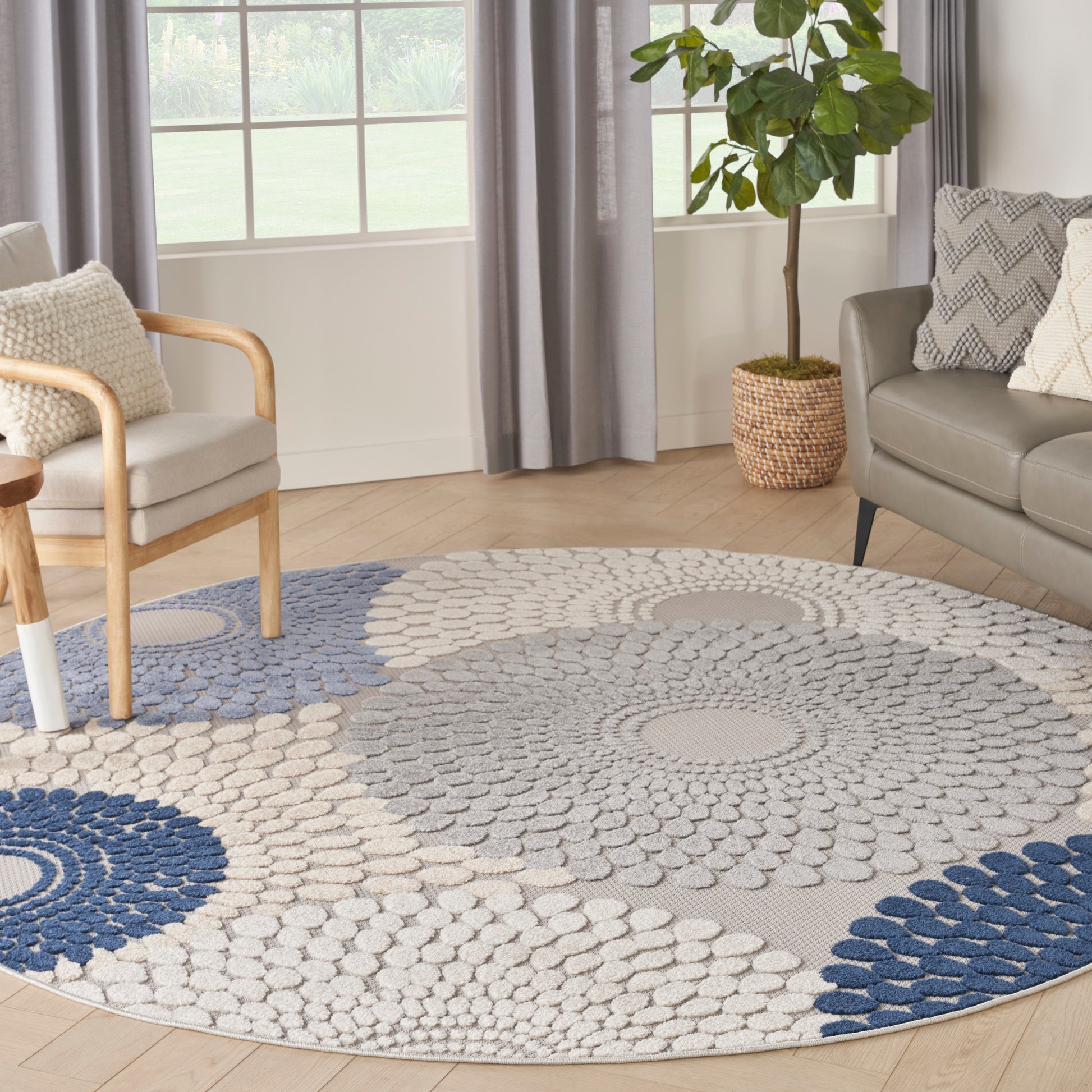 Round area rug with concentric blue and beige circles on light wood floor; modern living room with sofa, armchair, and plant.