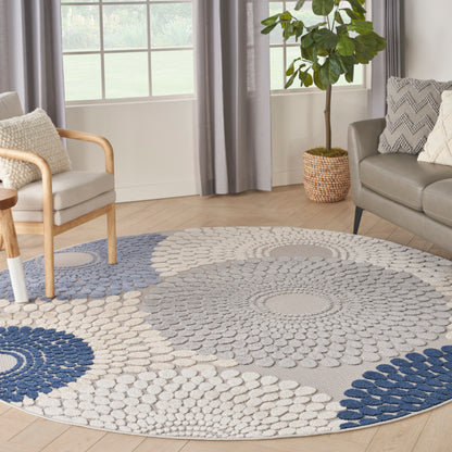 Round area rug with concentric blue and beige circles on light wood floor; modern living room with sofa, armchair, and plant.