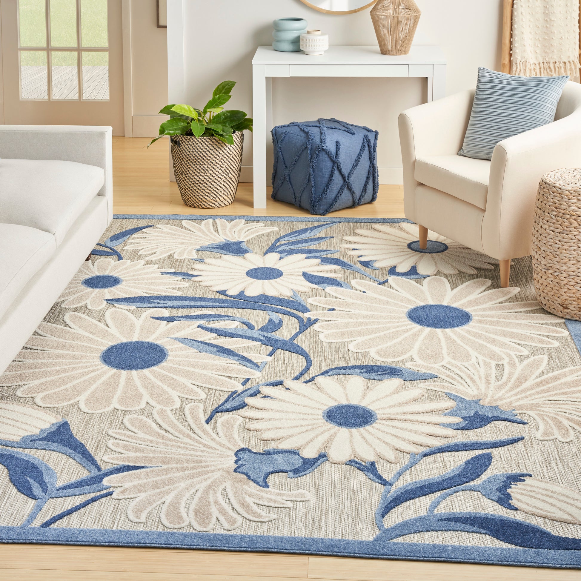 Floral area rug with oversized white-petaled daisies and blue centers on beige backdrop, blue border, in a bright living room.