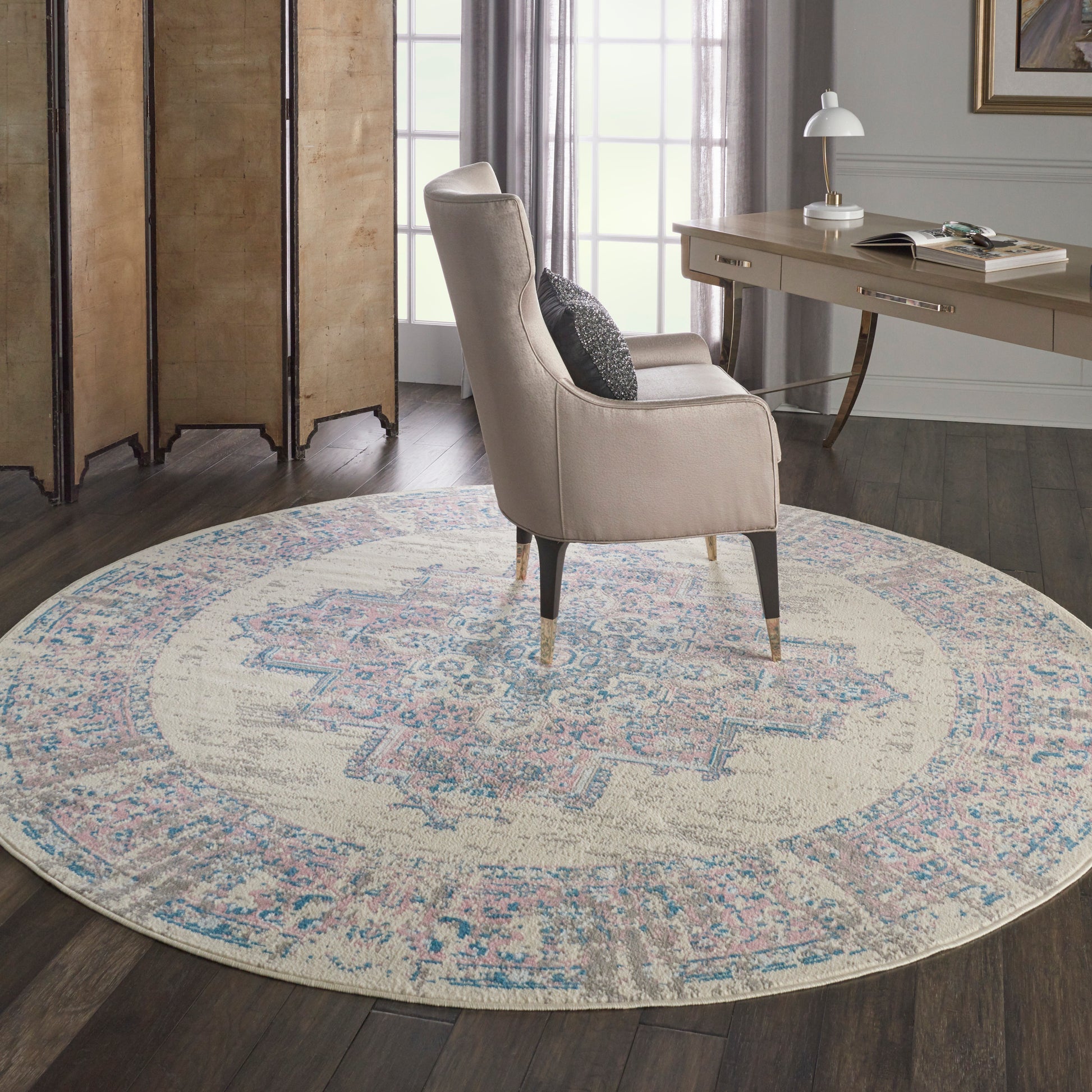 Beige curved-arm accent chair with dark tapered legs on a round pastel rug in a cozy home office.