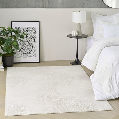 Neutral bedroom with white duvet, black nightstand and lamp, beige textured area rug, potted plant, and framed abstract art.