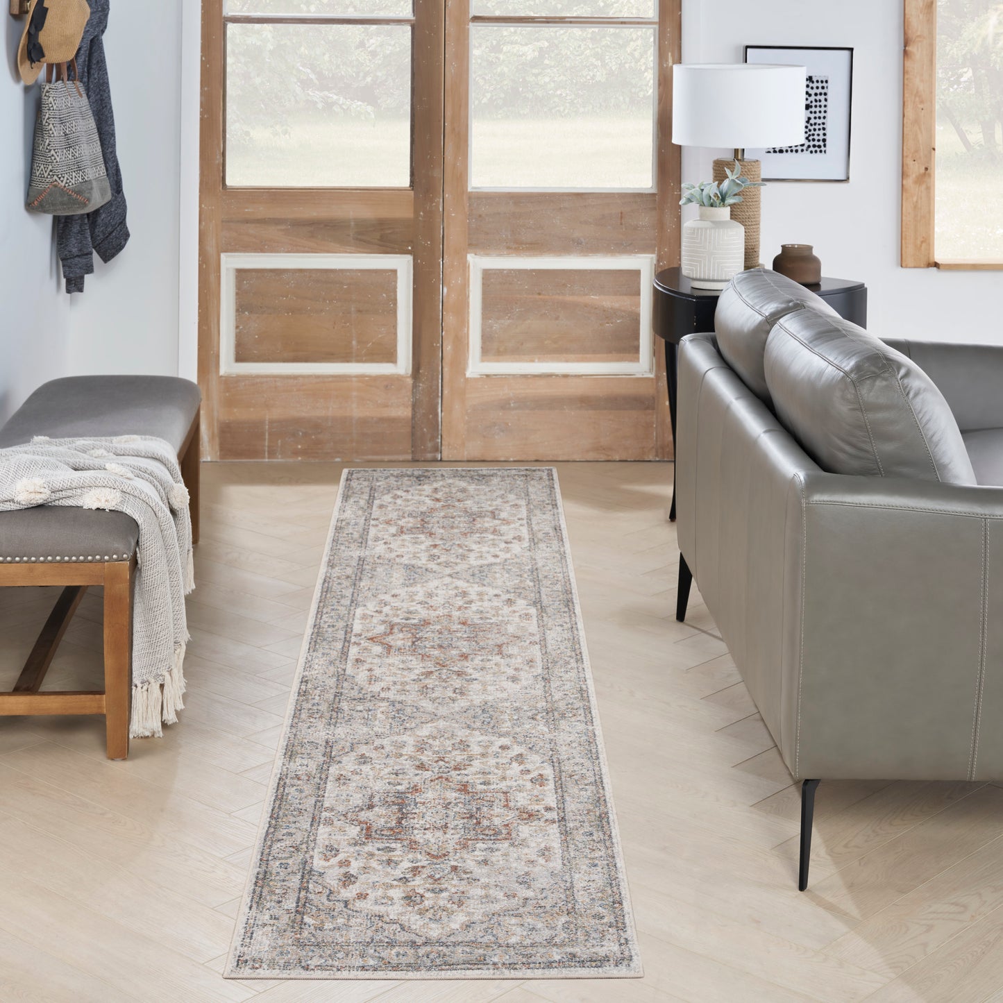 Light gray Persian-style rug runner with cream and rust motifs in a modern entryway beside a gray sofa.