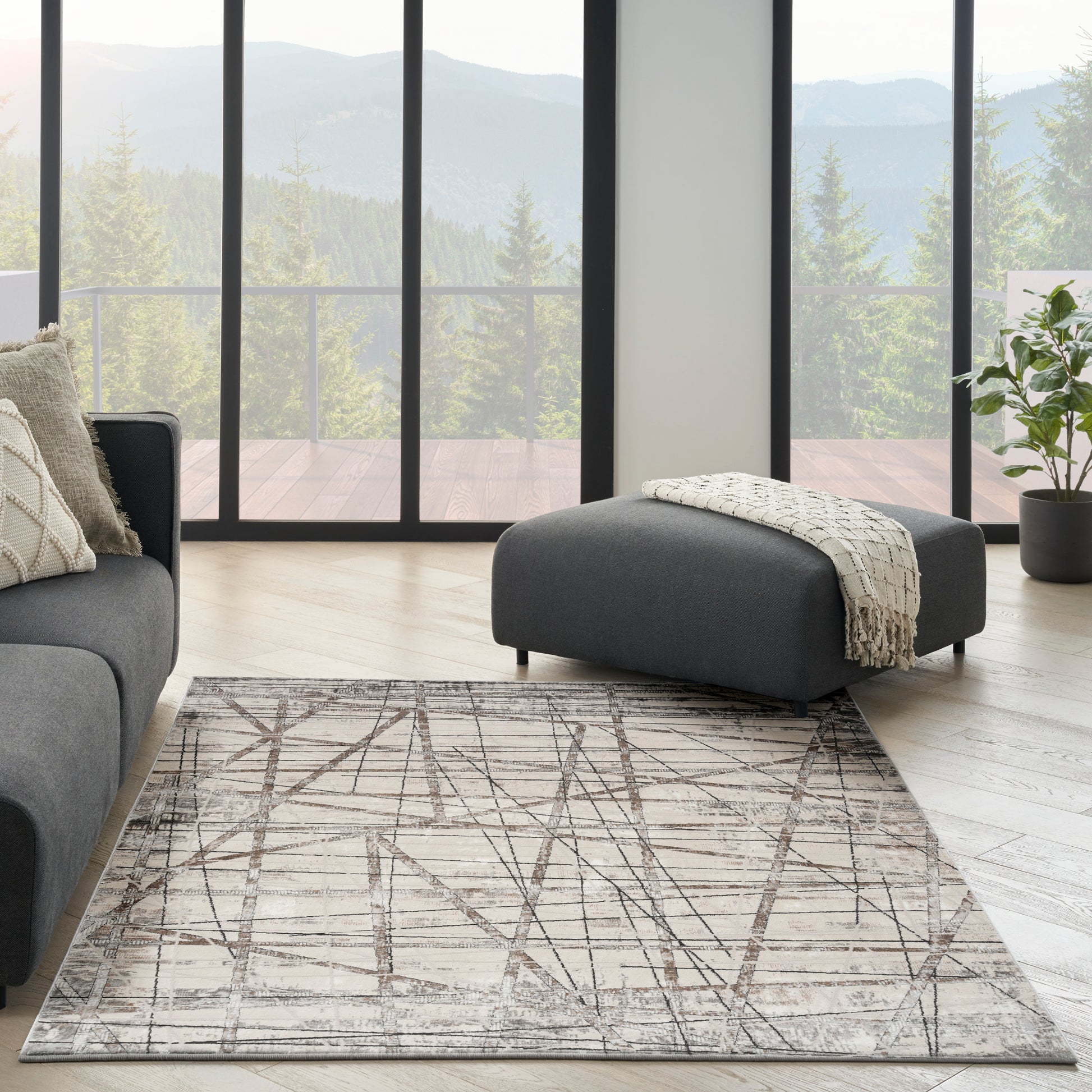 Modern living room with charcoal sofa, ottoman, beige geometric rug, light wood floor, and mountain view.