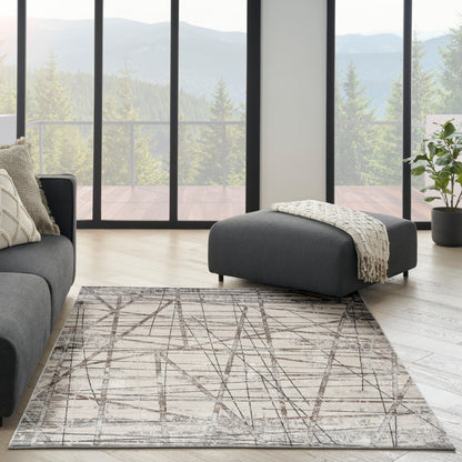 Modern living room with charcoal sofa, ottoman, beige geometric rug, light wood floor, and mountain view.