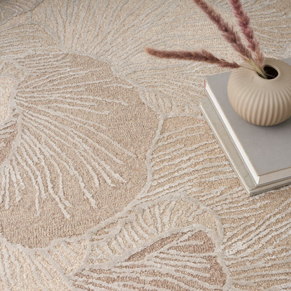 Beige textured rug with large leaf motif, paired with a ribbed cream vase, pampas grass, and stacked books.
