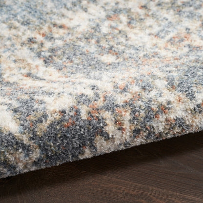 Close-up of a plush multicolor rug with blue, cream, gray and tan flecks on dark wood floor.