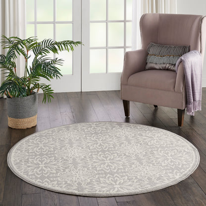 Round beige patterned area rug on dark wood floor, with pink upholstered wing chair and plant in woven basket.