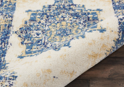 Blue & ivory distressed patterned area rug with tan accents, folded edge on dark wood floor.