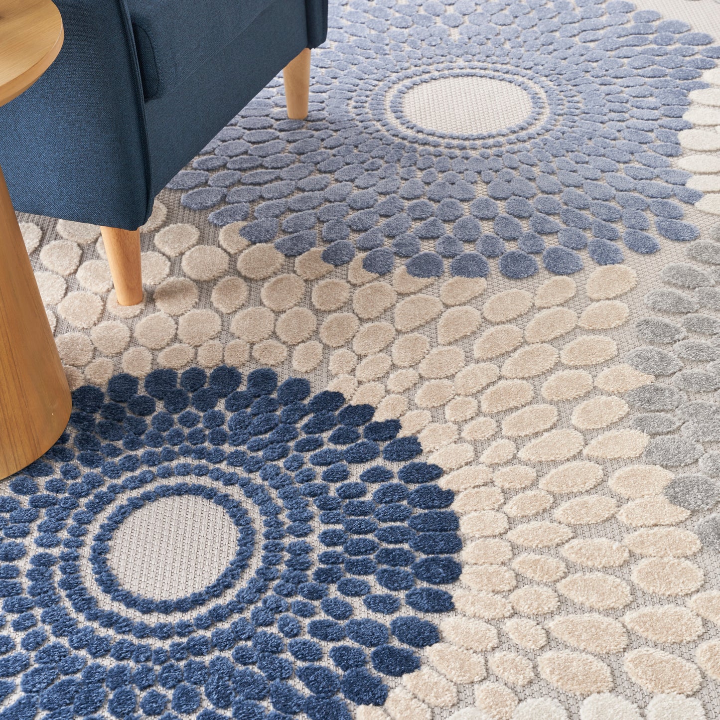 Textured circular pebble-pattern area rug in navy blue and beige under a blue sofa.